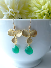 Load image into Gallery viewer, Gold earrings with green drops on a white cup with flowers in the background