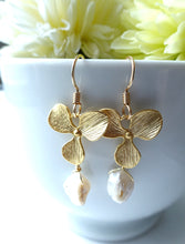 Load image into Gallery viewer, Gold leaf earrings with pearl drops in front of a white cup with yellow flowers.