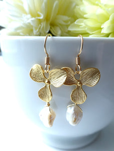 Gold leaf earrings with pearl drops in front of a white cup with yellow flowers.