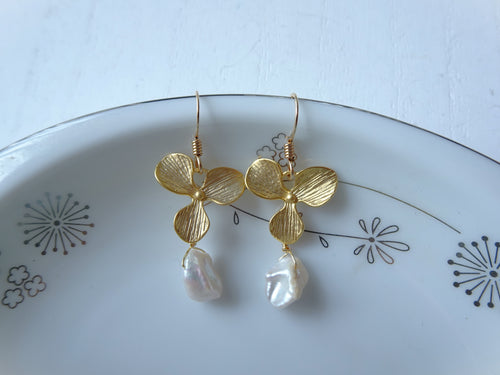 Gold butterfly earrings with pearl drops on a decorative plate.
