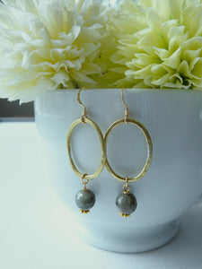 Gold hoop earrings with gray beads in front of light green flowers.