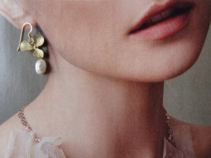 Close-up of a person wearing gold earrings with leaf design and pearl drop.