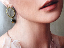 Load image into Gallery viewer, Close-up of a person wearing gold hoop earrings with a dark bead on a neutral background