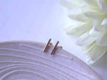 Load image into Gallery viewer, Gold stud earrings on a textured white surface with a white flower in the background