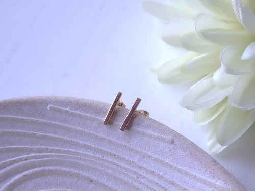 Gold stud earrings on a textured white surface with a white flower in the background