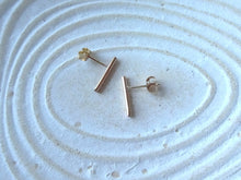 Load image into Gallery viewer, Gold bar earrings on a textured white surface