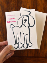 Load image into Gallery viewer, Greeting card with a dog illustration and text 'You're fabulous!' held by a hand on a wooden surface.