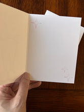 Load image into Gallery viewer, Hand holding a opened note card white pages featuring star designs on a wooden surface